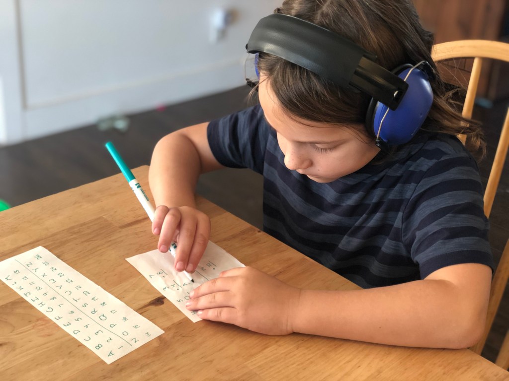Rondel sitting at the kitchen table with sound-reduction headphones, writing out the answer to one of his clues.